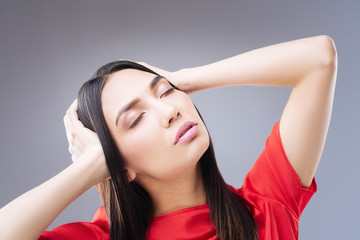 Fototapeta premium Unpleasant condition. Young lovely woman standing with her eyes closed and touching her head with two hands while feeling unwell and having an awful headache