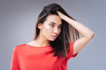 Fototapeta premium Wet hair. Emotional young woman looking unsatisfied while standing against the blue background and touching her wet hair after the rain
