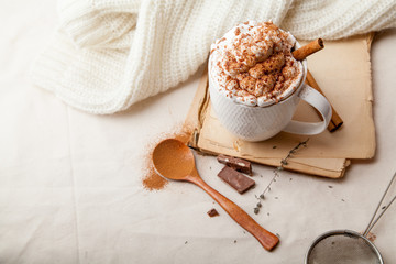 Cup of cocoa with cinnamon, whipped cream and chocolate. Textile background. Scandinavian winter concept. Horizontal composition with copy space.