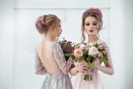 Two bride girls with hairdos with colored strands holding bouquets of flowers in their hands.