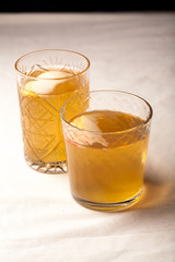 Two vintage glasses with apple cider on black background. Christmas beverages concept. Two red apples and rosemary sprig aside.  Warm backlight. Vertical composition.