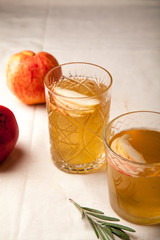 Two vintage glasses with apple cider on black background. Christmas beverages concept. Two red apples and rosemary sprig aside.  Warm backlight. Vertical composition.