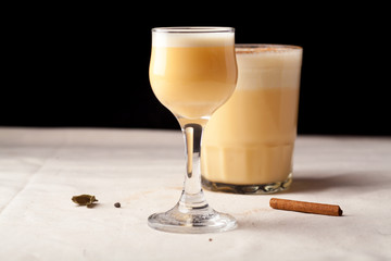Two glasses with christmas eggnog drink decorated with cinnamon on dark background. Horizontal composition with copy space.