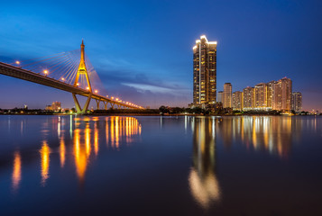 Fototapeta na wymiar Bhumibol Bridge, the Industrial Ring Road Bridge with skyscraper in the night scene after sunset. Twilight sky and light reflection on smooth water, Thailand