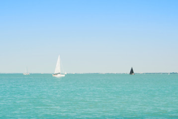 Bright blue transparent lake river water with white and black yachts at the horizon on sunny summer day.