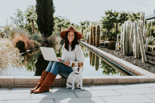 .Pretty young woman working outdoors with her adorable dog jack rusell in a park surrounded by cactus and a small pond.