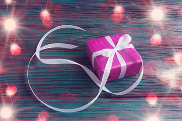 Pink gift box with long ribbon over old wooden background