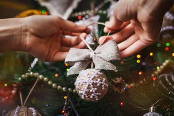 Hipster hands with Christmas ball and bow and tree background. xmas decorations with toys, sparkling, glowing. Happy New Year and Xmas theme