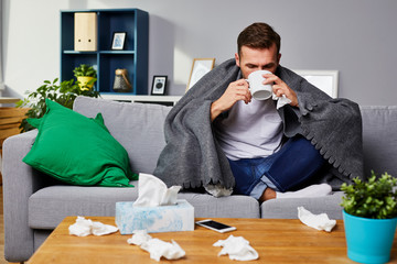 Ill man drinking hot tea sitting on sofa at home