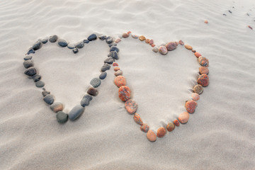 Pebbles arranged in shape of two hearts on sand beach ripples
