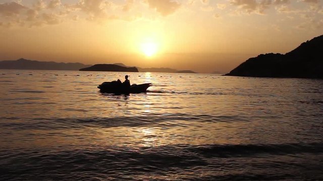 A silhouetted pedalo crosses a peaceful bay ast he sun sets over the Greek island of Kalymnos.