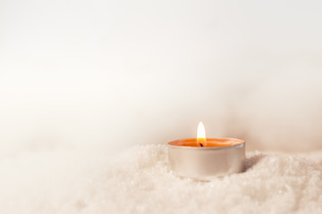 Brennendes Teelicht im Schnee mit wei&szlig;em Hintergrund und Lichter Bokeh