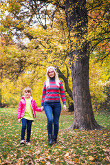 Mother and daughter walking trough forest in fall