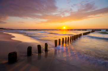 sunset over the sea beach, waves crashing on the stakes