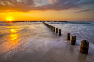 Fototapeta na wymiar sunset over the sea beach, waves crashing on the stakes