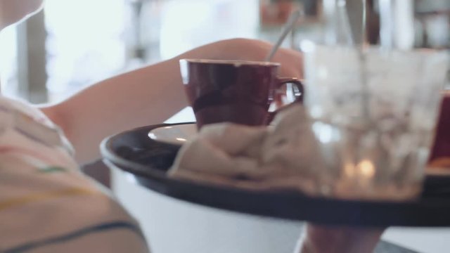 Camera follows female waiter while she carries tray full of dirty plates, cups and cuttlery to bar or kitchen. restaurant and hotel business, busy lunch break or brunch time in hipster cafe