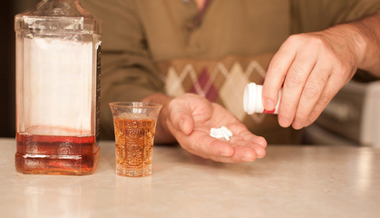 A person holding a glass of alcohol and a handful of pills.