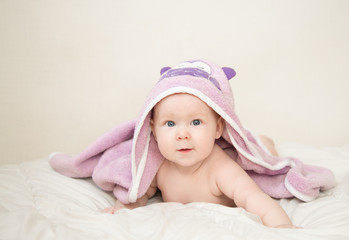 Beautiful smiling cute baby girl after a bath under the towel on the bed in the room at home. Happy child smiling.