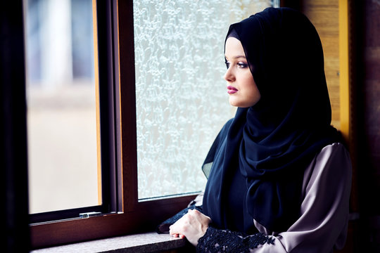 young woman wearing hijab looking out the window at mosque