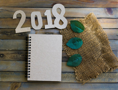notepad with number paper 2018 and leaf on wood background for happy new year image. And welcome new year photo.