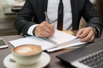 businessman writes in a notebook while sitting at a desk in coffee shop