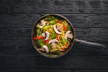 Noodles with vegetables in a frying pan. Asian Cuisine Pasta. Top view. Free space. On a wooden background.;