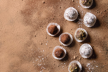 Variety of homemade dark chocolate truffles with cocoa powder, coconut, walnuts over cocoa powder as background. Top view, copy space.