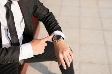 Businessman sitting at train station is looking at watch.  he looks on the time and hurrying in a rush hour to work. Hurry time.