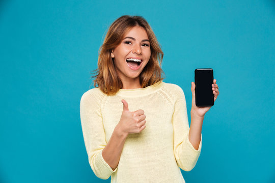 Happy woman in sweater showing blank smartphone screen