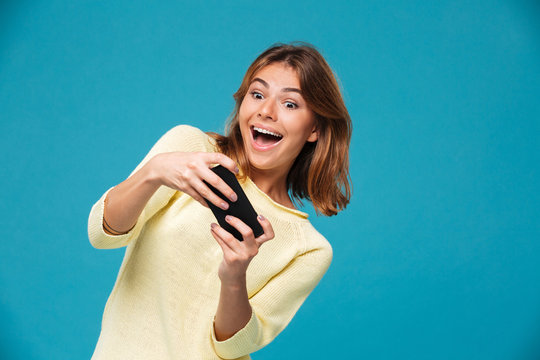 Happy playful woman in sweater playing on smartphone