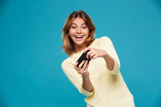 Surprised happy woman in sweater playing on smartphone