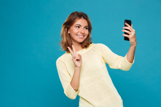 Smiling woman in sweater making selfie on smartphone