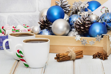 Decorative balls and pine cones in a wooden box and two white cups of coffee. The concept of Christmas and New Year.