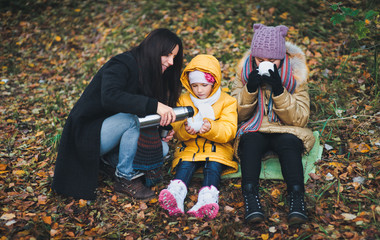 On an autumn walk Mom pours warm tea from her thermos to her daughters. The concept of a family walk.