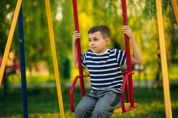 A little boy in a striped T-shirt is playing on the playground, Swing on a swing. Child is smiling and cheering