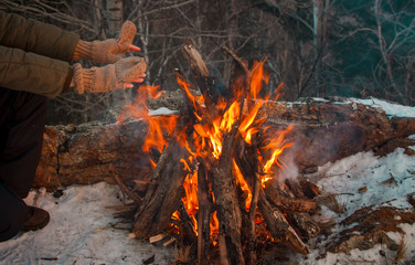 A couple is warming on a small fire after a hike through the winter forest