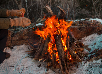 A couple is warming on a small fire after a hike through the winter forest