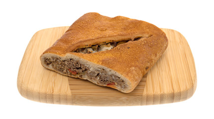 A large slice of a baked steak stromboli on a wood cutting board isolated on a white background.