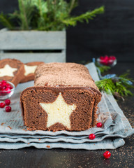 A very chocolate cake covered with dark chocolate and sprinkled with cocoa with a vanilla star inside. On a wooden dark background. Decorated with fresh cranberries, The perfect cool Christmas dessert