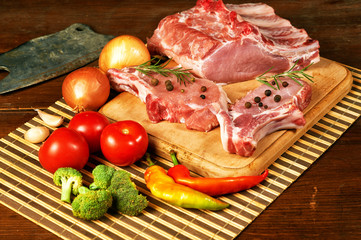 Raw steak , chops, meat with spices and vegetables on wooden table