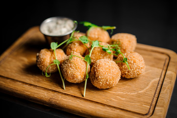 Tasty cheese balls decorated with green and sauce served in the wooden plate