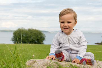 The boy is sitting on a stone with a view of the beautiful coast