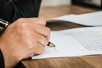 Close up business woman signing terms of agreement document on wooden table, signing concept