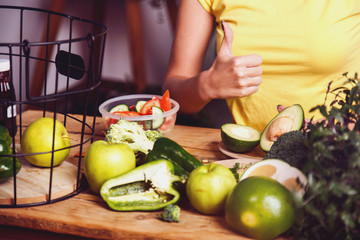 Smiling girl shows thumb up sign at the table with lots of healthy food