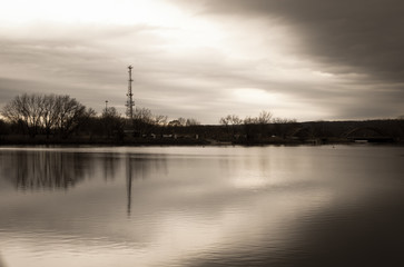 Obraz premium Lake background with moody cloud and sky water reflection. River front with bridge background. Cellular radio tower with overcast moody sky background. Parks and recreation outdoor design. 
