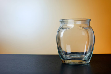 Empty glass jar on black table with orange background