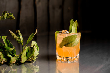Glass of orange alcoholic drink with ice decorated with salvia leaves