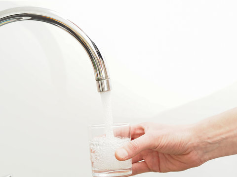 Hand hält Glas unter Wasserhahn