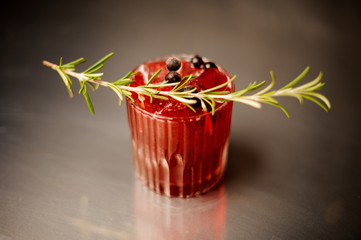 Glass of a red alcoholic cocktail decorated with a sprig of rosemary and black currant berries