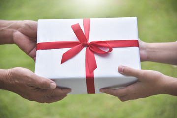 Closeup on hands Asian woman giving a white gift box to elderly man on green nature background for Birthday, Christmas and New year on white background.